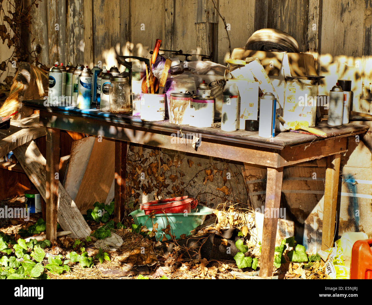 Mesa de trabajo antiguo cubierto con pintura y suministros fuera un rústico establo Foto de stock
