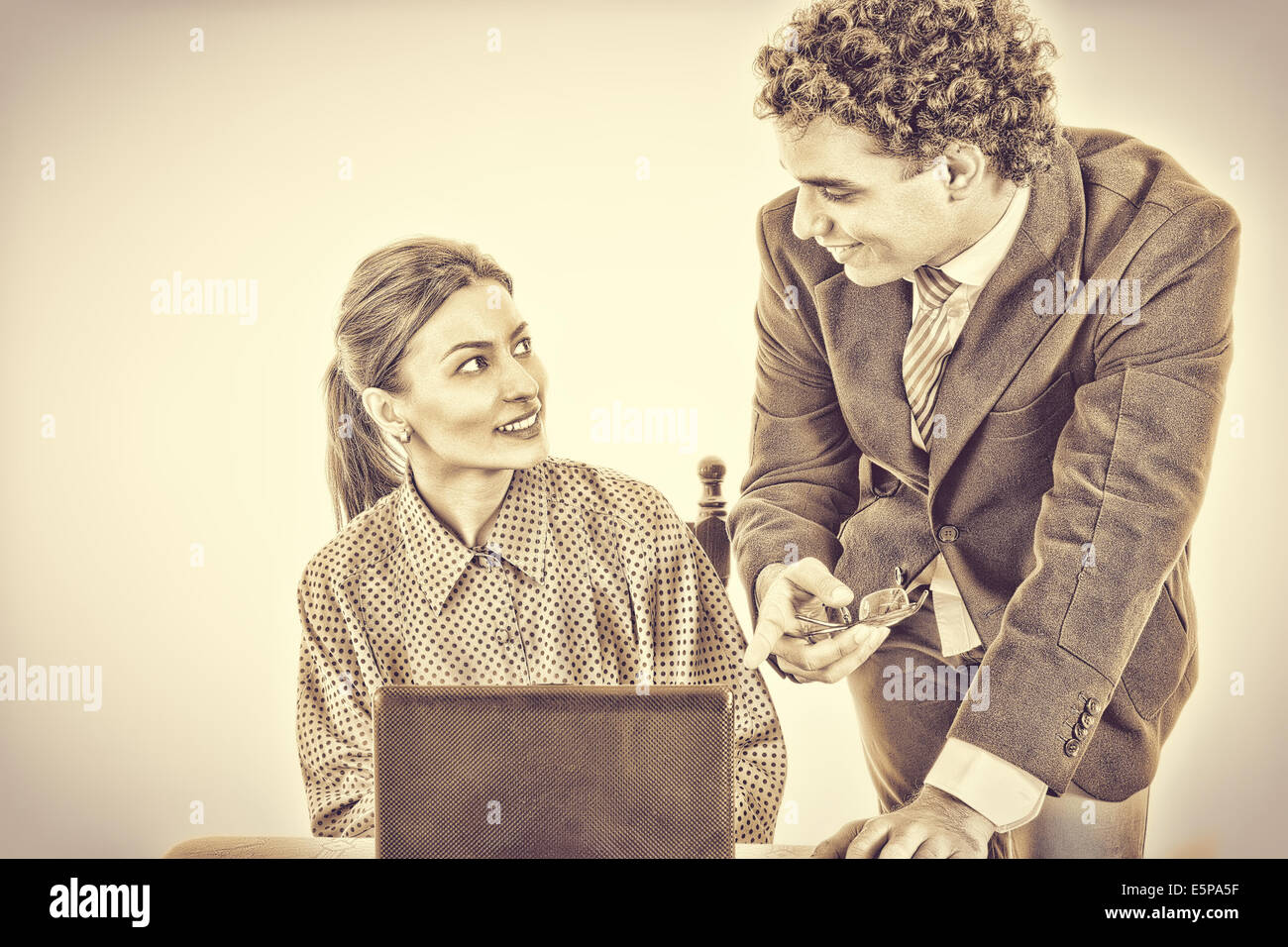 Jefe satisfecho y sonriente secretario trabajando juntos en equipo portátil, mostrando algo en la pantalla, en blanco y negro estilo vintage Foto de stock