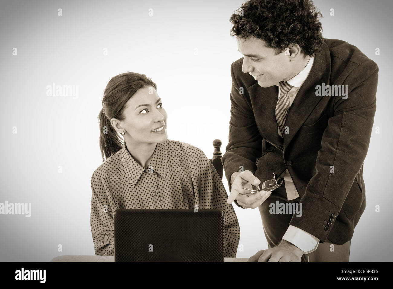 Jefe satisfecho y sonriente secretario trabajando juntos en equipo portátil, mostrando algo en la pantalla, el negro y el blanco de estilo Foto de stock
