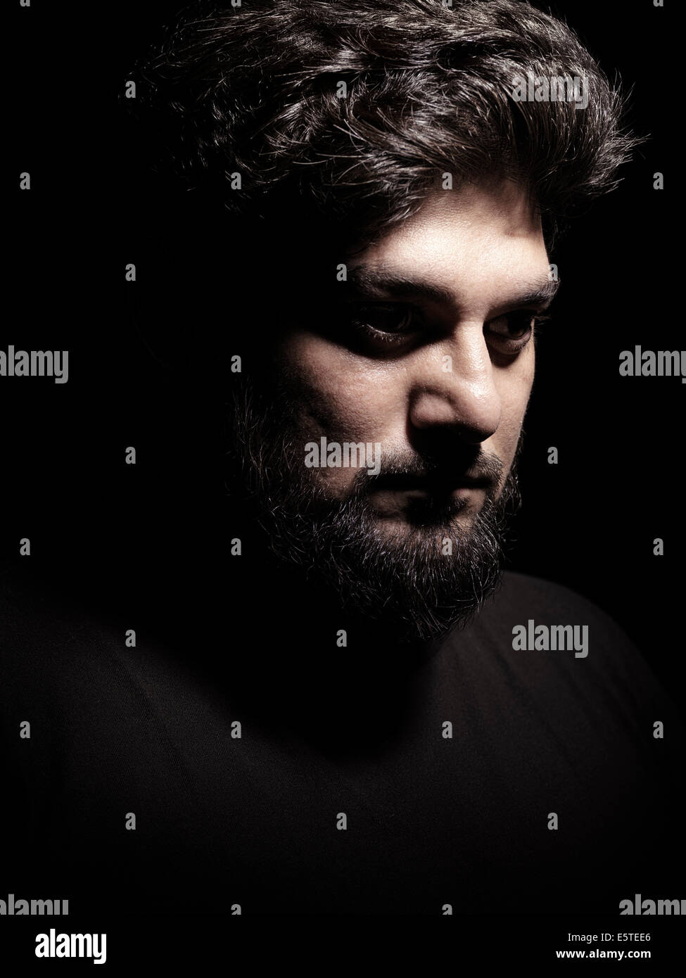 Dramático expresivo retrato de un hombre de Oriente Medio thoughful con fuertes sombras aislado sobre fondo negro Foto de stock