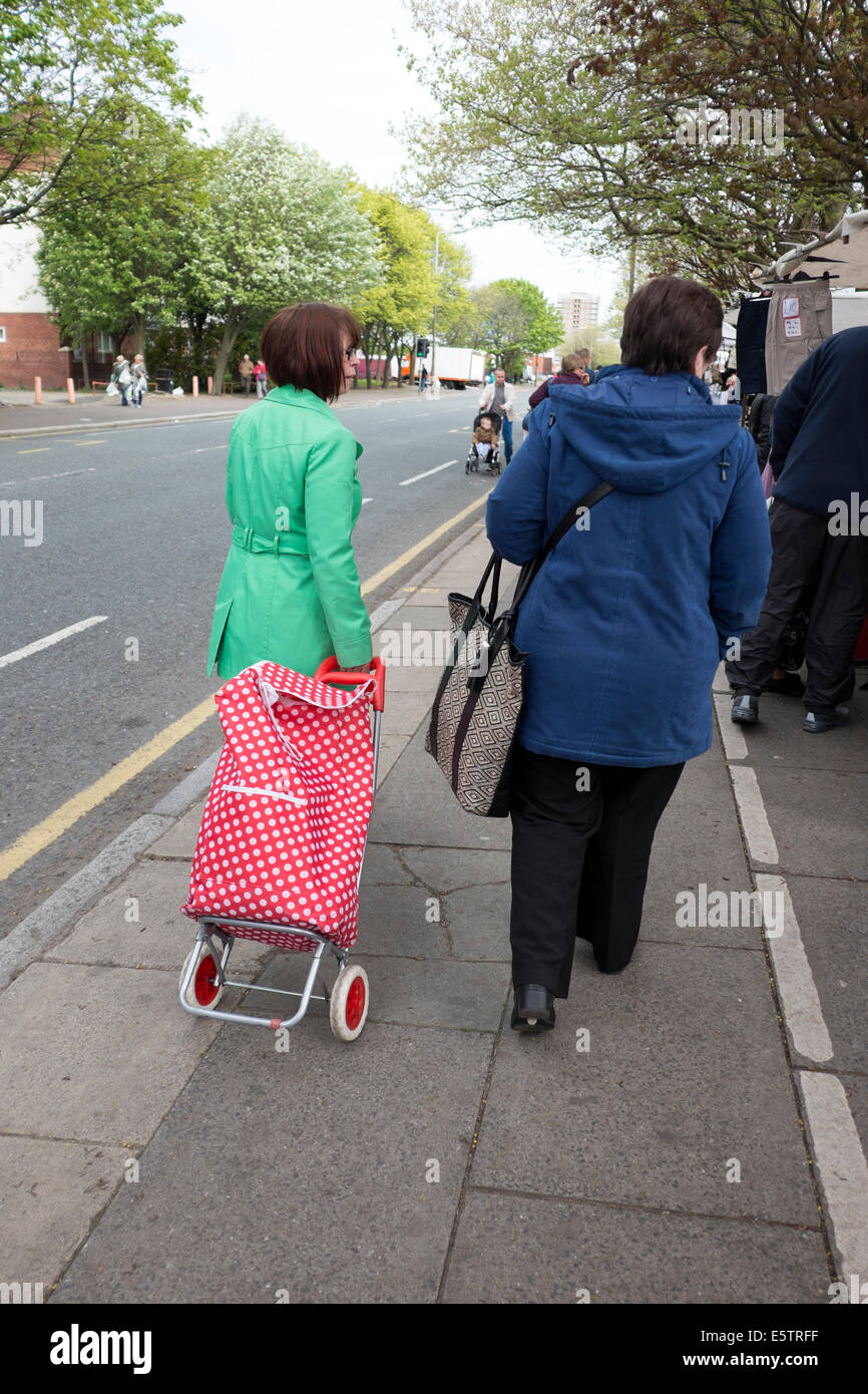 Mujer con abrigo rojo verde brillante tirando irregular Carrito de compras Foto de stock
