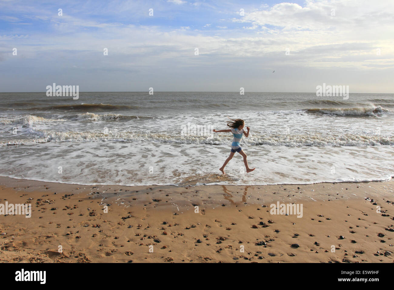 Niña que corre a lo largo de arena, en la costa oriental de bach.Norfolk, UK Foto de stock