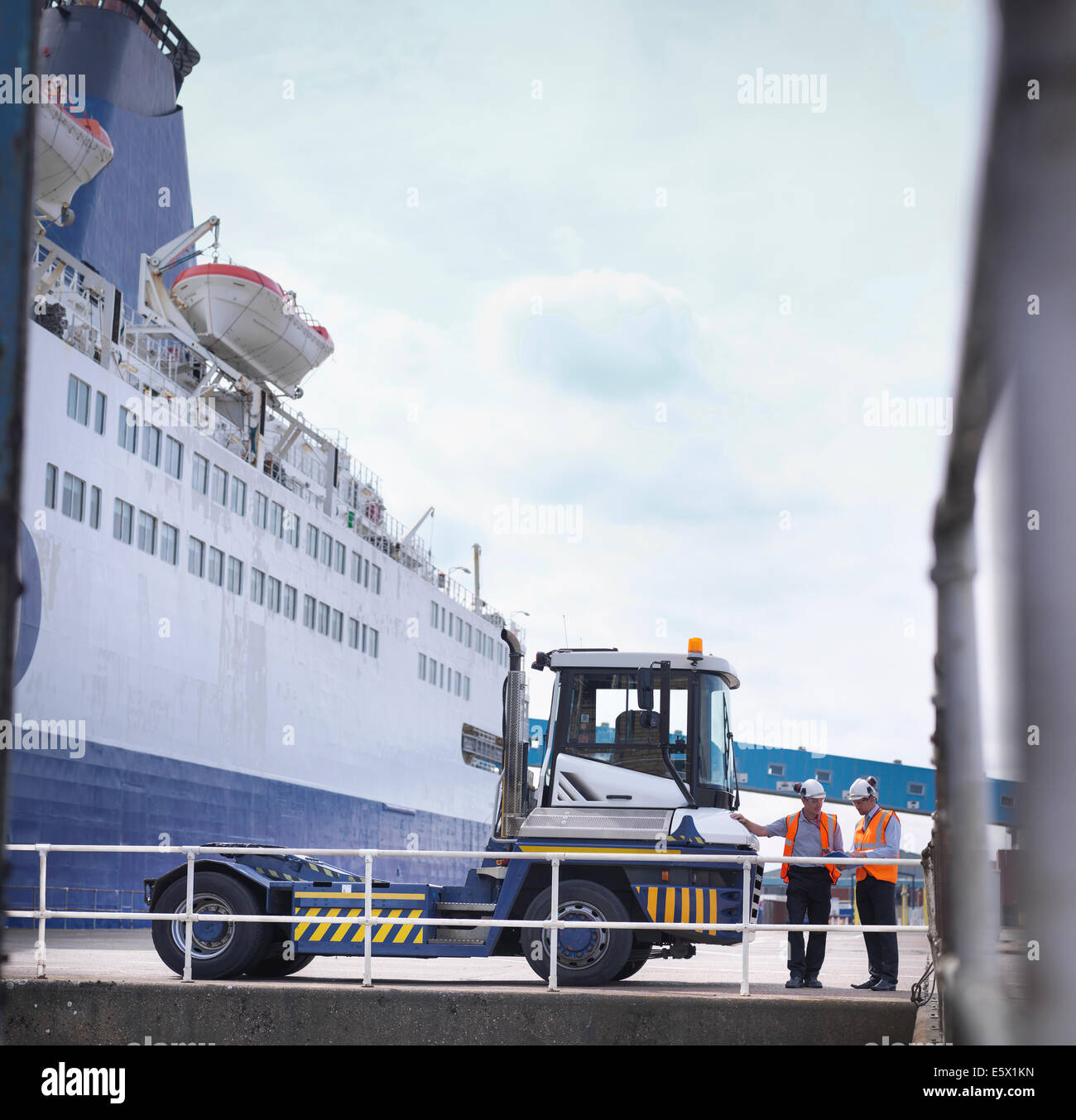 Los trabajadores portuarios con camión contenedor de envío y el buque en el puerto Foto de stock