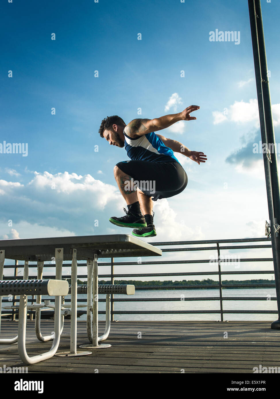 Joven saltando hacia atrás desde la mesa de picnic en el lago pier Foto de stock