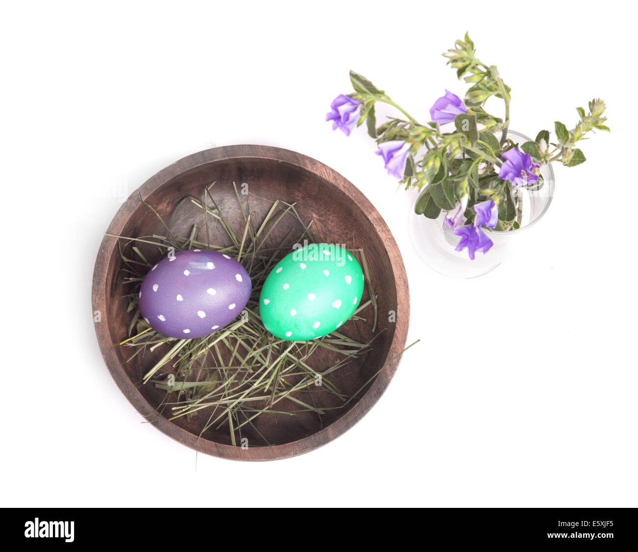 Los huevos de Pascua en un recipiente de madera y flores sobre fondo blanco. Foto de stock