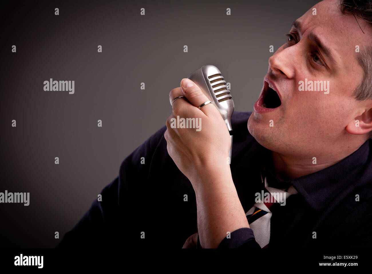 Un estilo de cincuenta cantante es cantar con un micrófono viejo en su mano Foto de stock