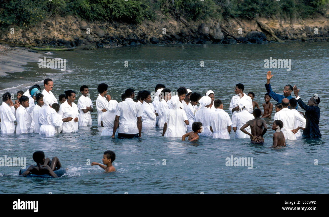 Los participantes religiosos vestidos de blanco para el bautismo por inmersión completa en el agua fuera de Martinica, una isla en el Mar Caribe. Foto de stock