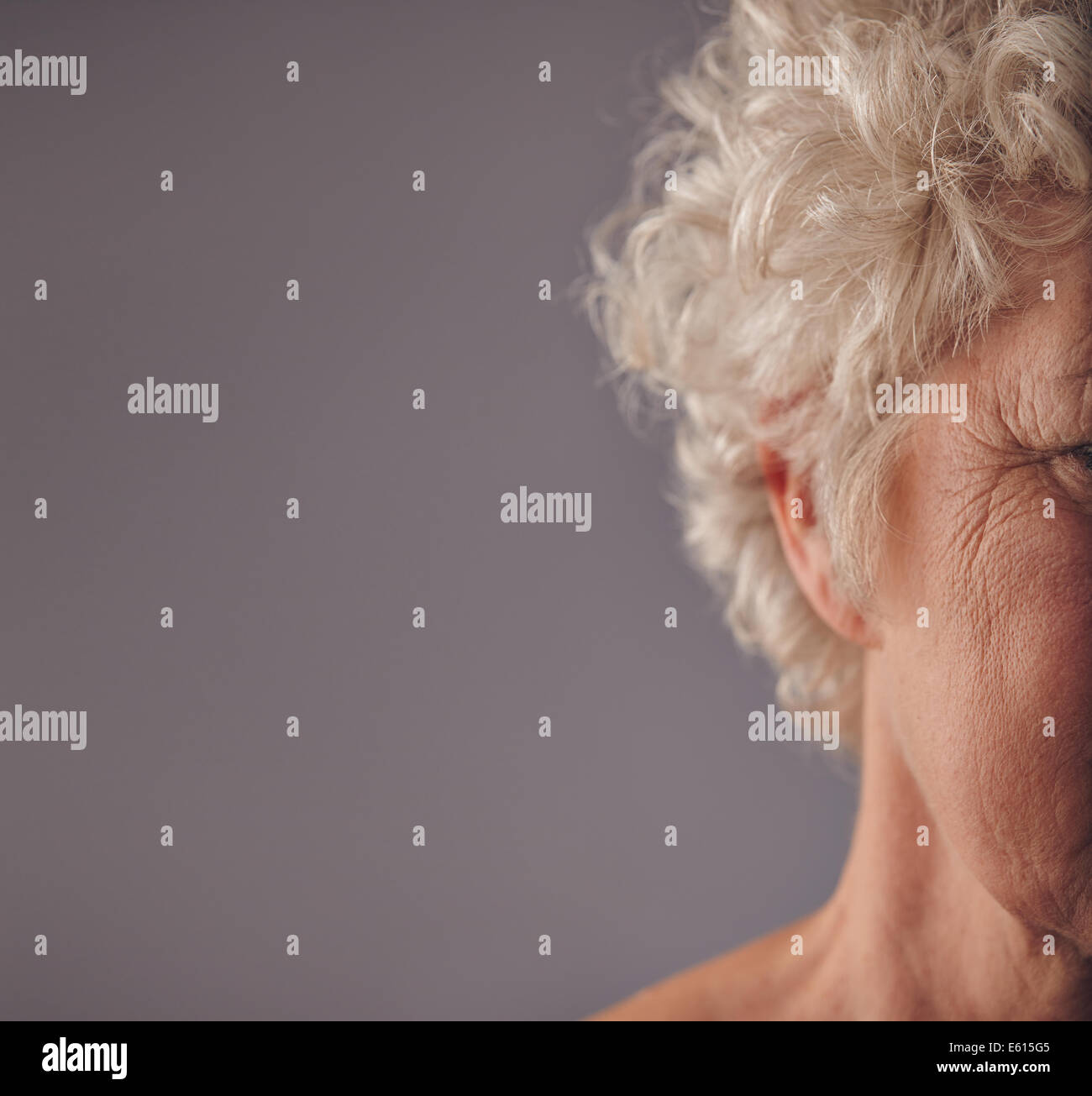 Imagen recortada de la mujer de más edad se enfrentan con piel arrugada sobre fondo gris. Patas de gallo en los ojos de la anciana. Foto de stock