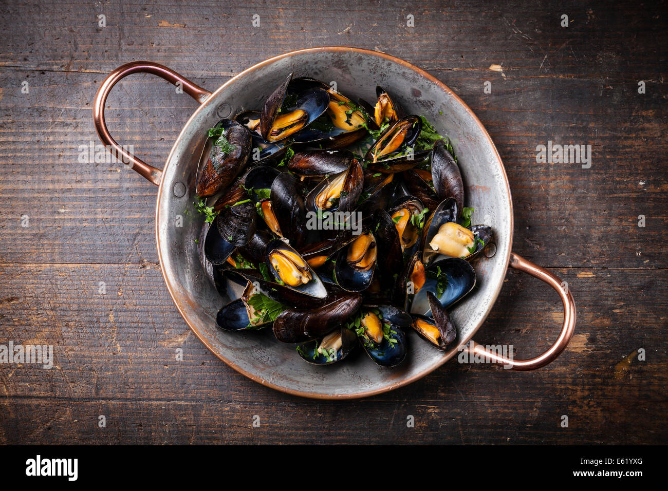 Mejillones hervidos en plato de cocina de cobre sobre fondo de madera oscura. Foto de stock