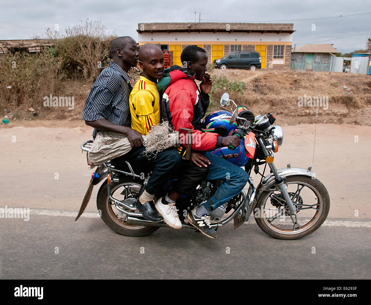 Ciclo motor sobrecargado taxi con tres hombres dos pasajeros en Namanga Nairobi Kenya África carretera MOTOCICLETA TAXI OVERLO SOBRECARGA Foto de stock