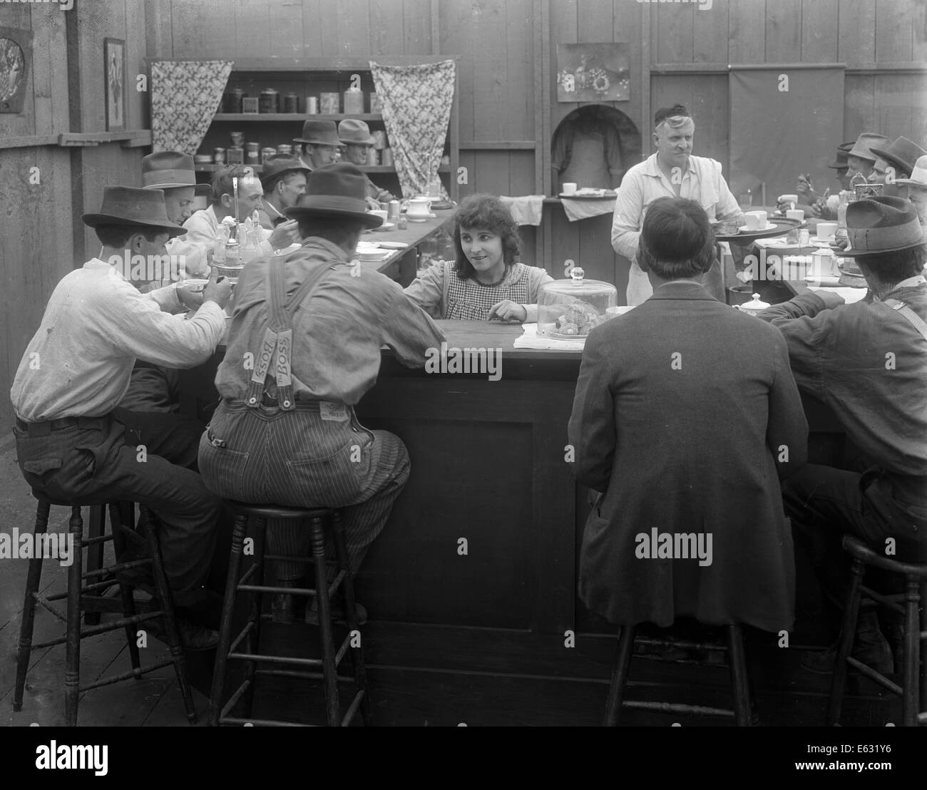 1900 1910s mujer esperando a los clientes sentados alrededor de contador en restaurante Diner película todavía silenciosa Foto de stock