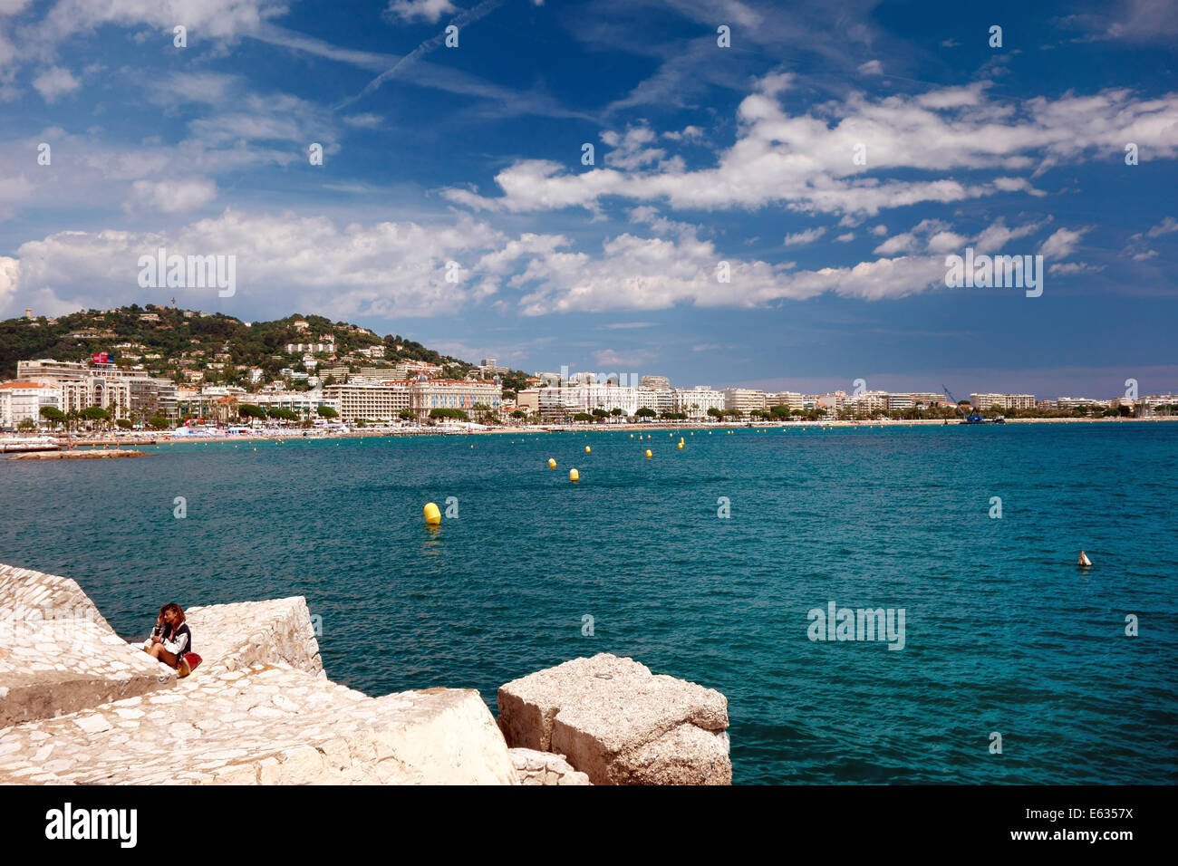 Chica sentada sobre las rocas con paseo marítimo de Cannes en segundo plano. Foto de stock