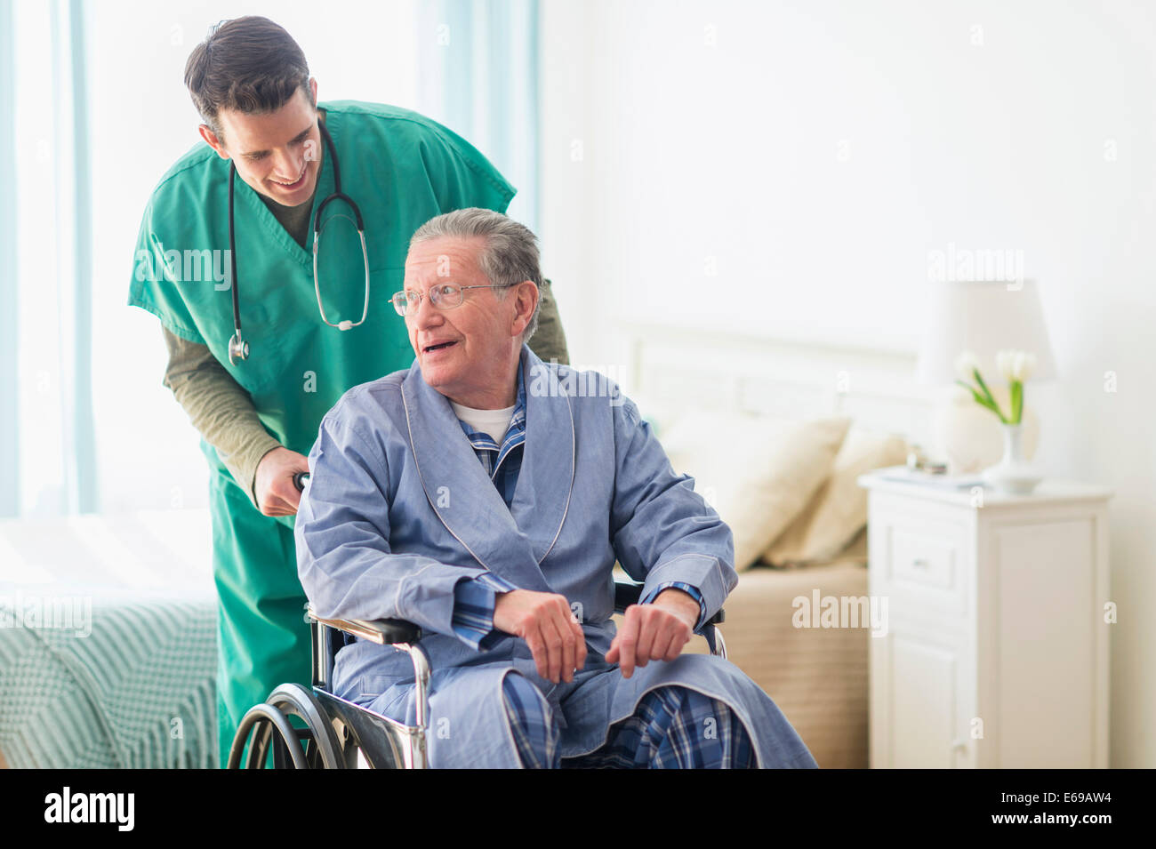 Enfermera caucásica wheeling paciente en casa Foto de stock