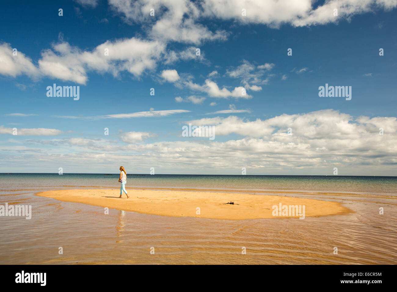 Una niña teeneage en una isla de arena siendo cortado por la marea entrante en baja en Newton, Northumberland, Reino Unido. Foto de stock