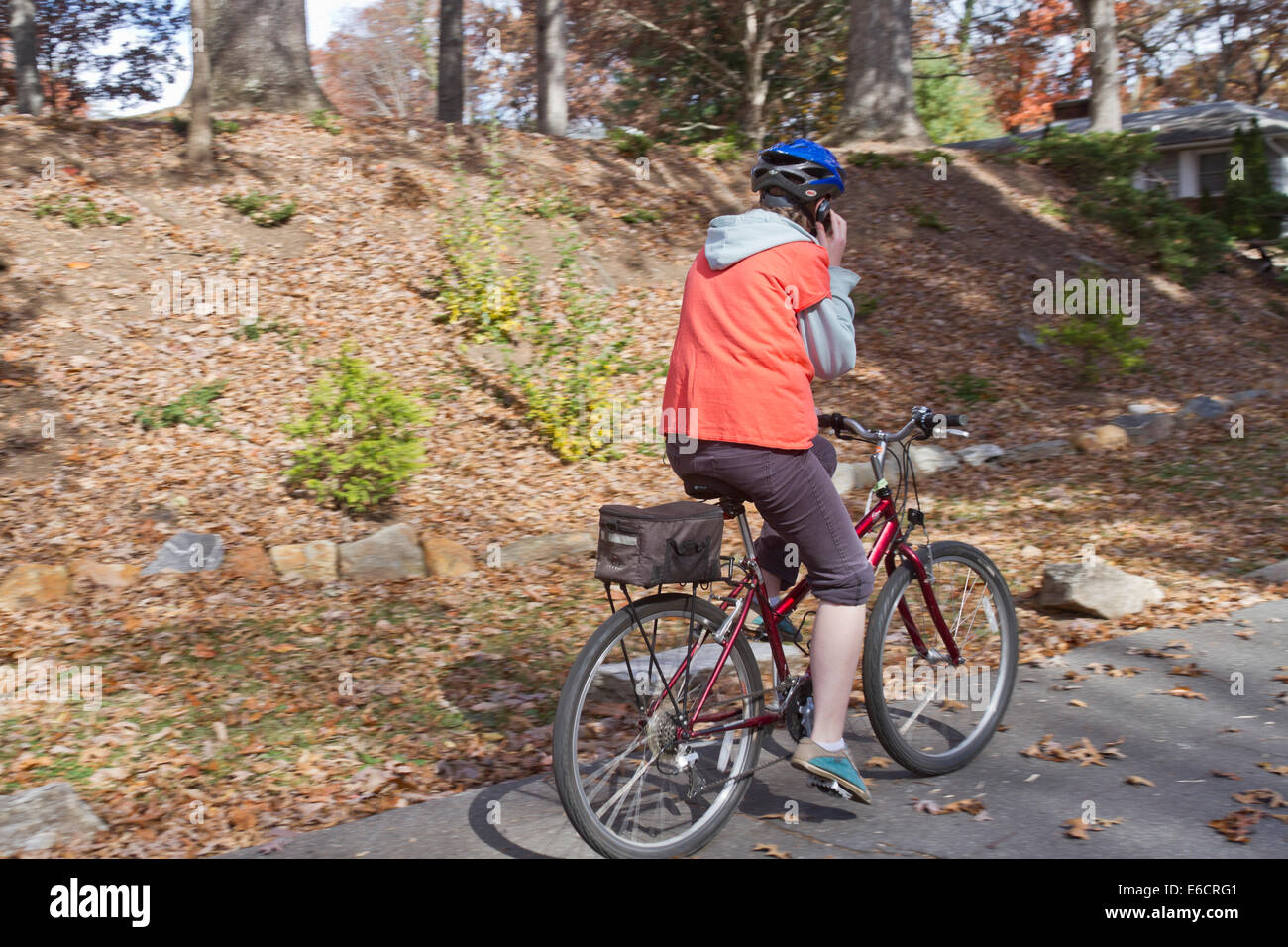 Mujer joven hablando por un teléfono celular mientras viajaba en una bicicleta y no prestar atención al hermoso paisaje otoñal a su alrededor. Foto de stock