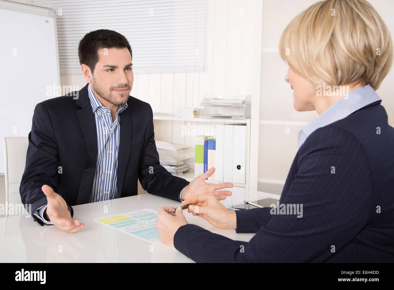 Entrevista de trabajo o una reunión situación: hombre y mujer de negocios sentado en un escritorio explicando algo. Foto de stock