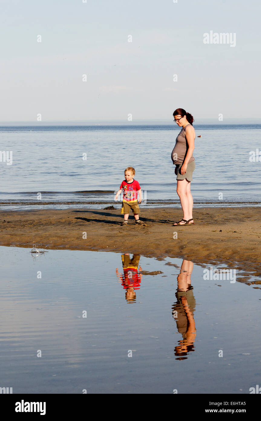 Una madre y su hijo se refleja en el agua quieta en la playa Foto de stock