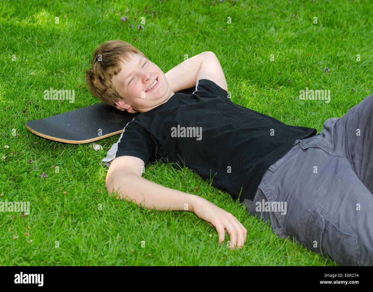 Laughing guy relajarse en monopatín en park hierba y descansar después de un ocio activo Foto de stock