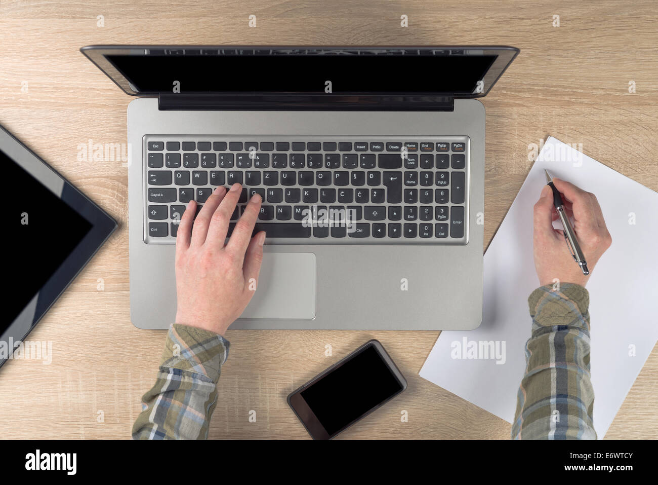 Programador femenino escribir notas sobre el trozo de papel mientras escribe el teclado portátil, vista superior. Foto de stock