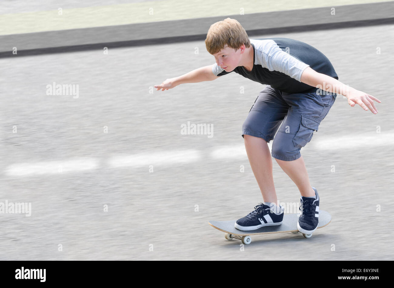 Joven patinador adolescente guy in motion moviendo en patineta a lo largo de calzada contra el asfalto borroso fondo con espacio de copia Foto de stock