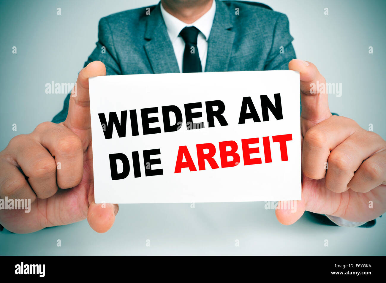 Empresario sosteniendo un cartel con el texto wieder an die arbeit, de vuelta al trabajo en alemán, escrito en él Foto de stock