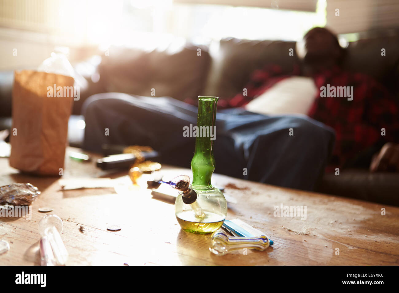 El hombre se desplomó en el sofá con parafernalia de drogas en primer plano Foto de stock