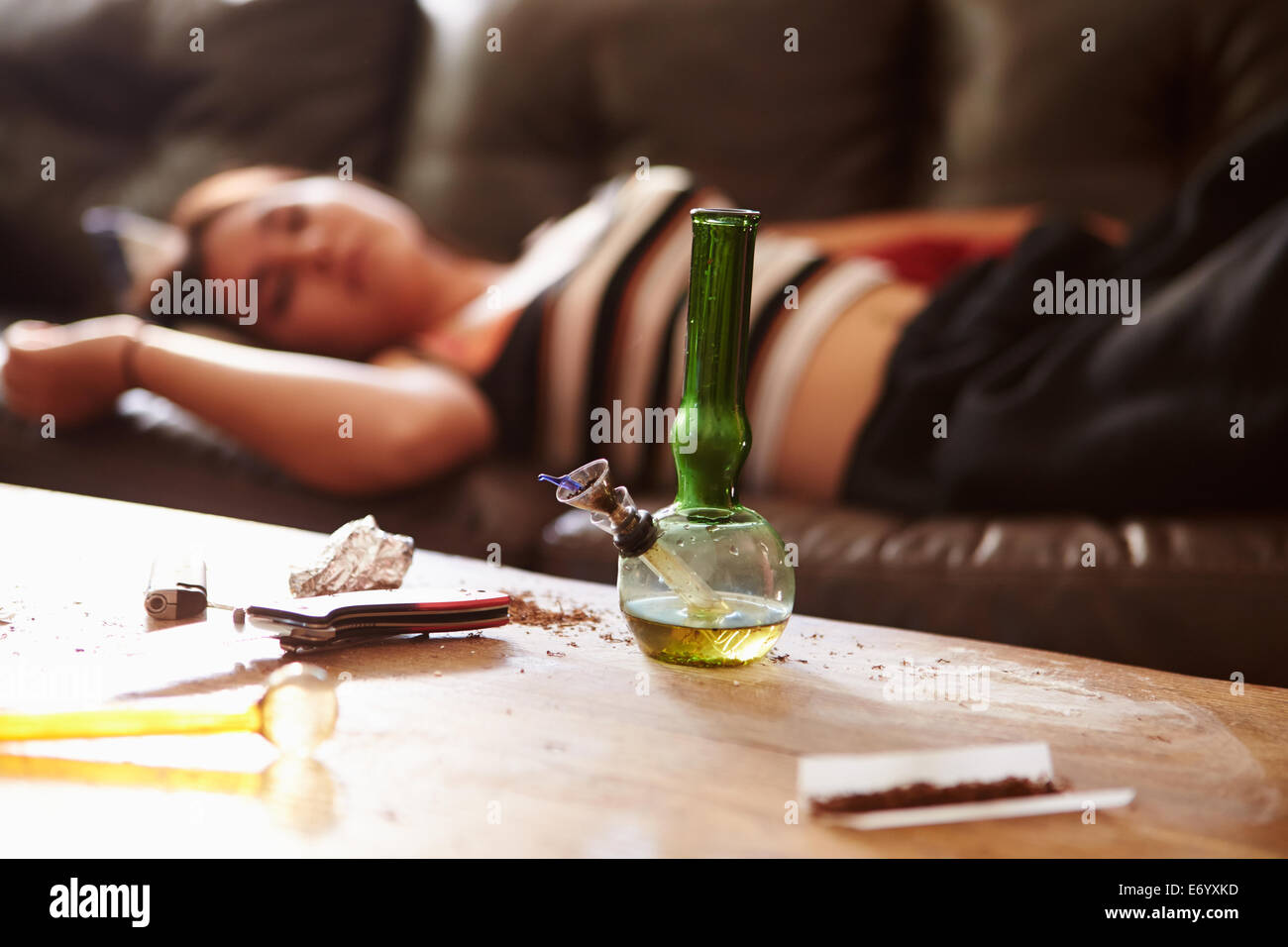 La mujer se desplomó en el sofá con parafernalia de drogas en primer plano Foto de stock