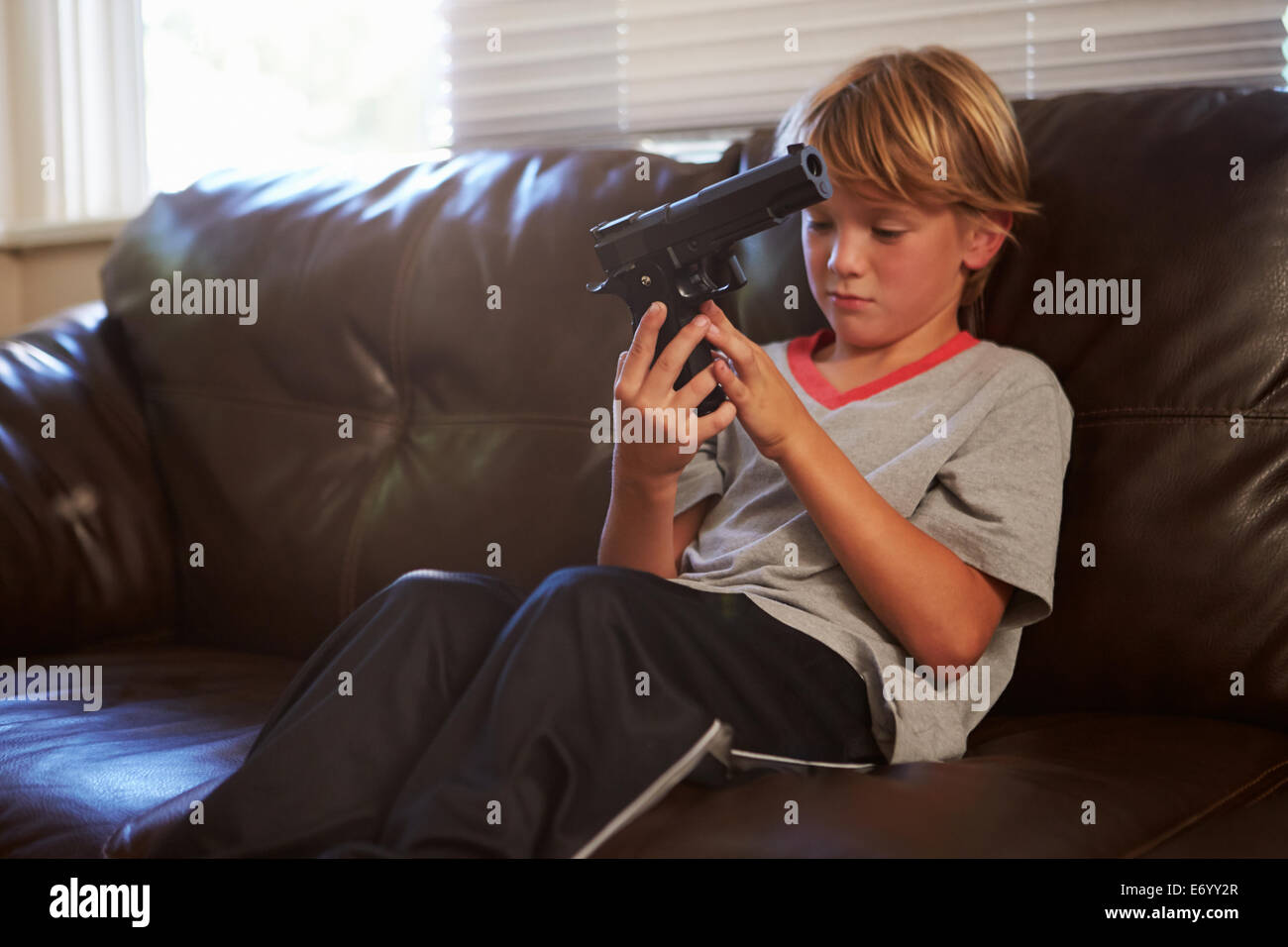 Niño jugando con la pistola del padre que ha encontrado en su casa Foto de stock