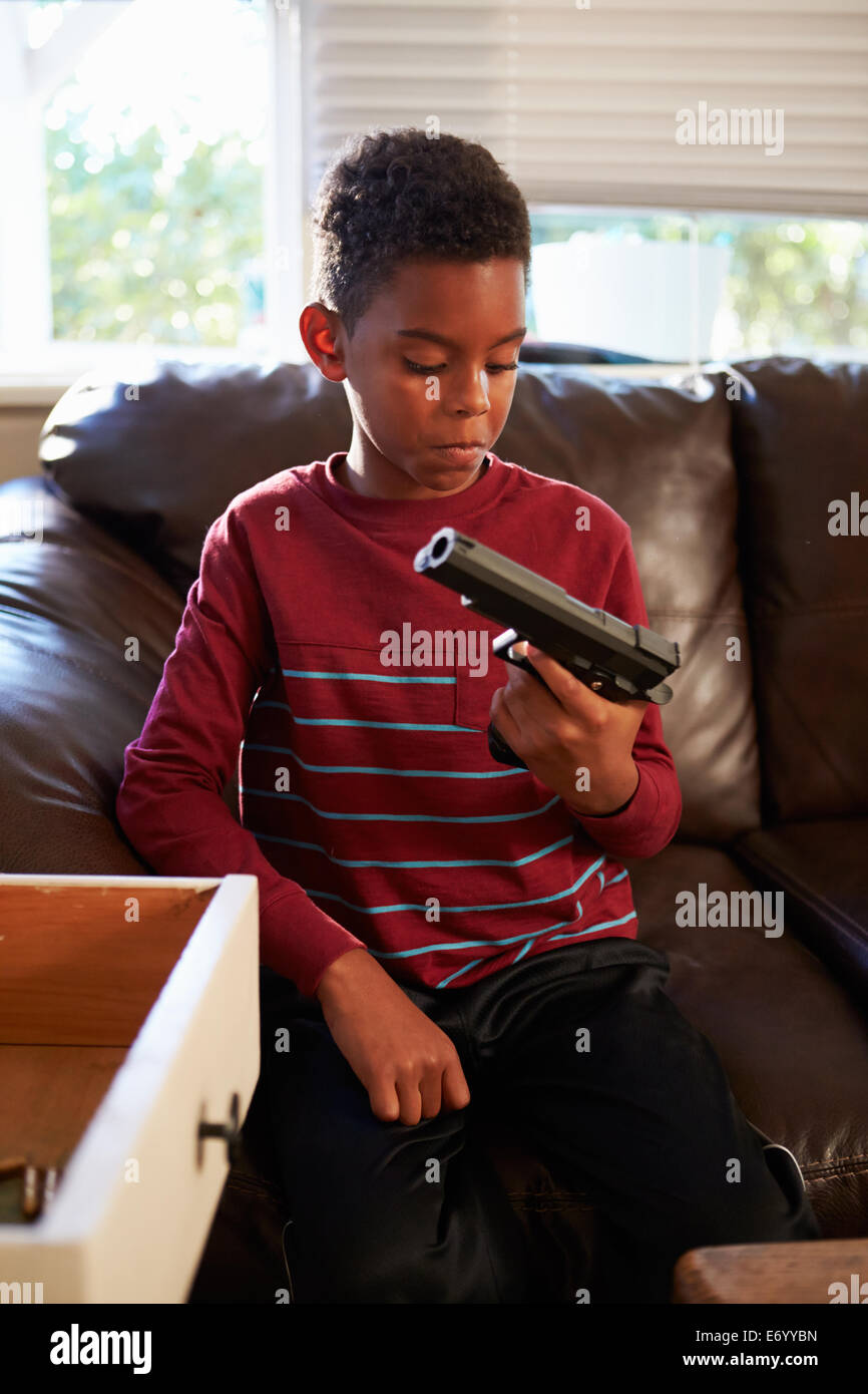 Niño jugando con la pistola del padre que ha encontrado en su casa Foto de stock