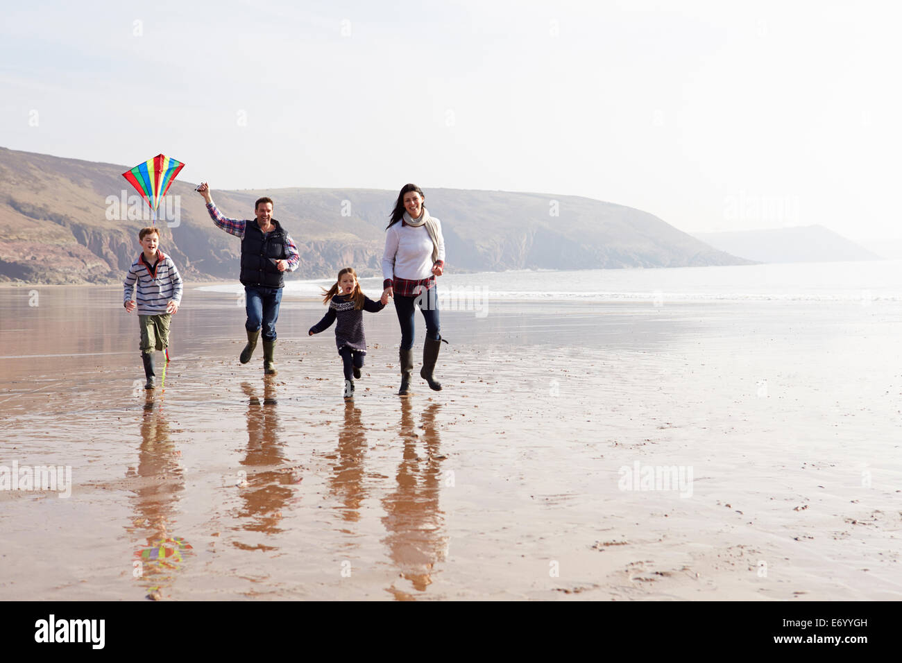 Familia que corre a lo largo de invierno volar cometas en la playa Foto de stock