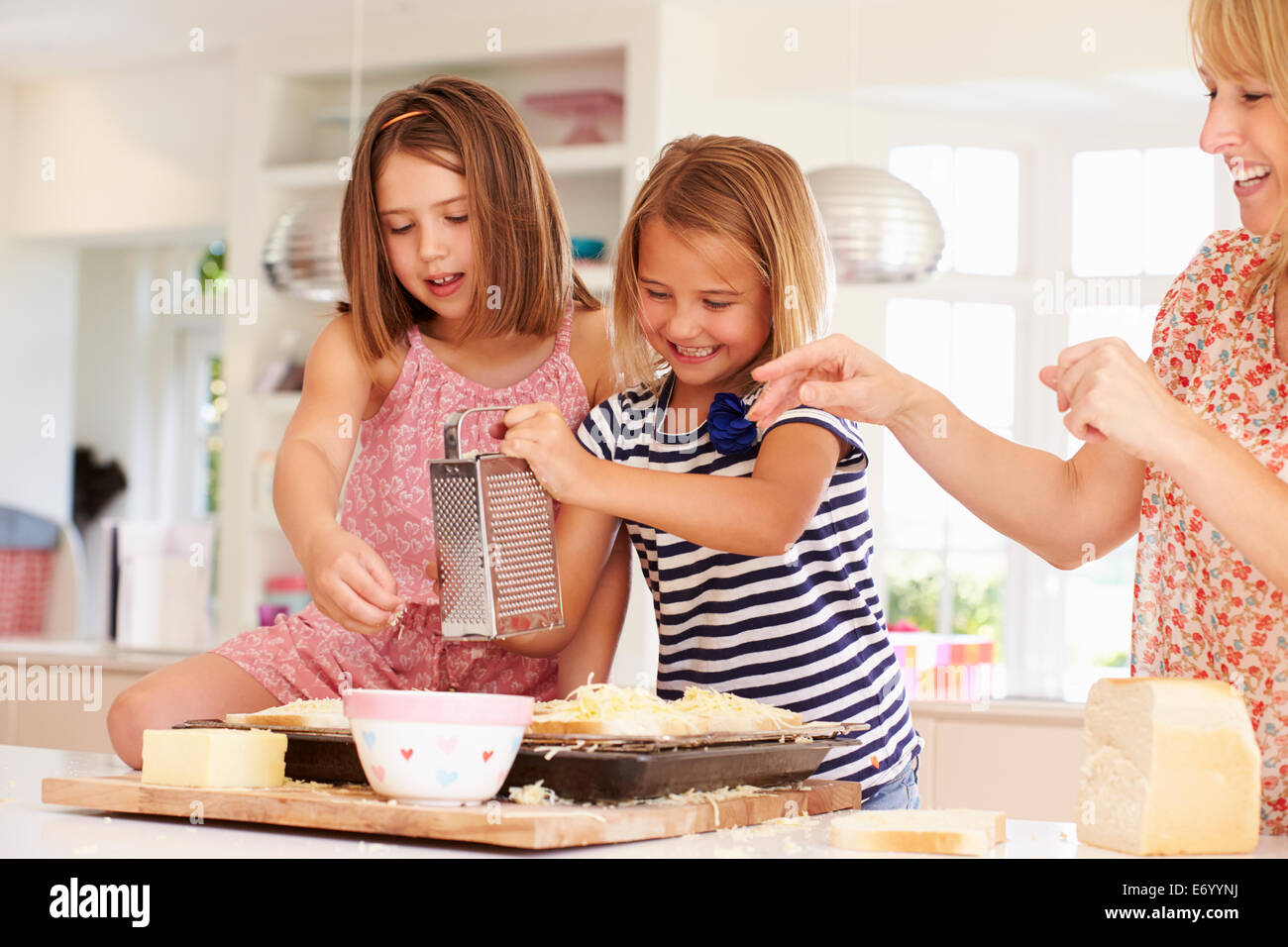 Las niñas con la madre haciendo queso sobre tostadas Foto de stock