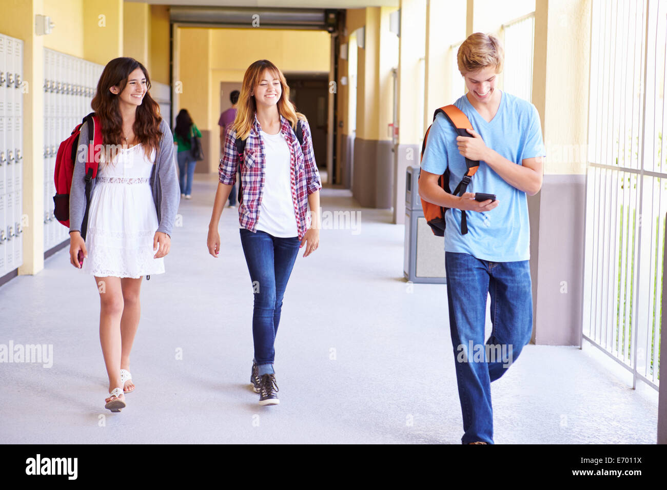 Los estudiantes de secundaria caminando en el pasillo a través de teléfono móvil Foto de stock