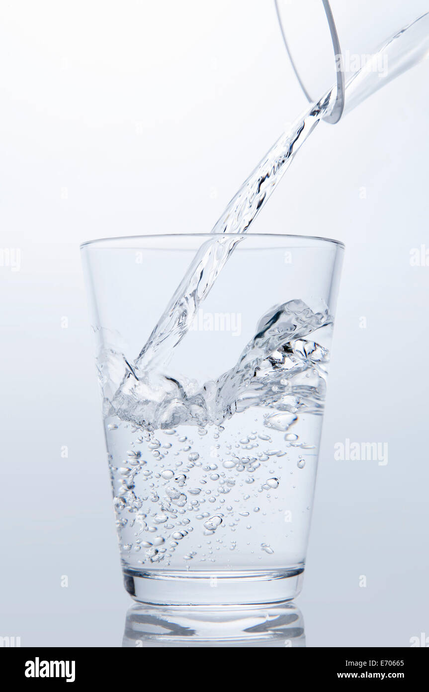 Verter agua clara desde la jarra en el vaso para beber Foto de stock