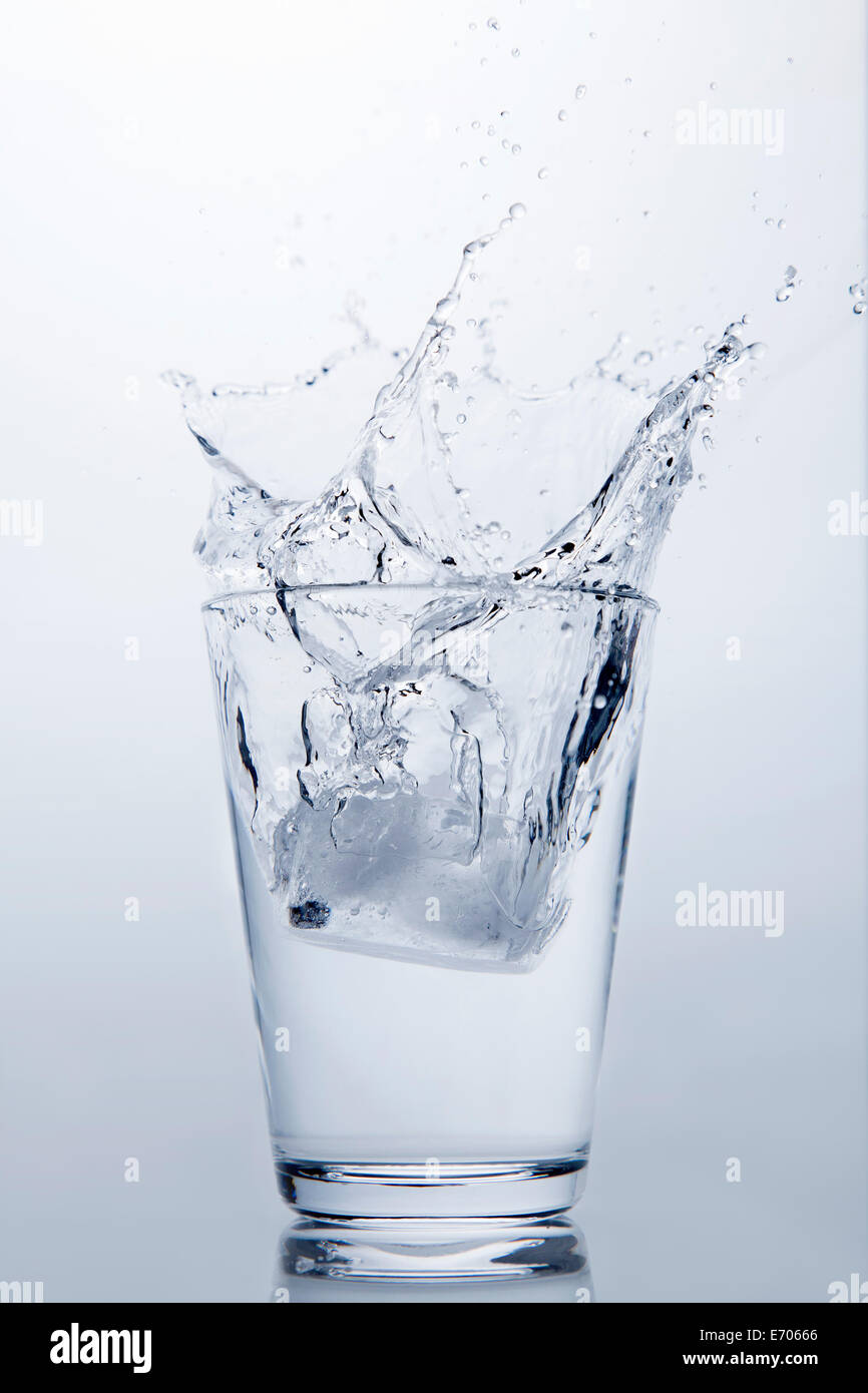 Cubo de hielo que cae en un vaso de agua clara Foto de stock