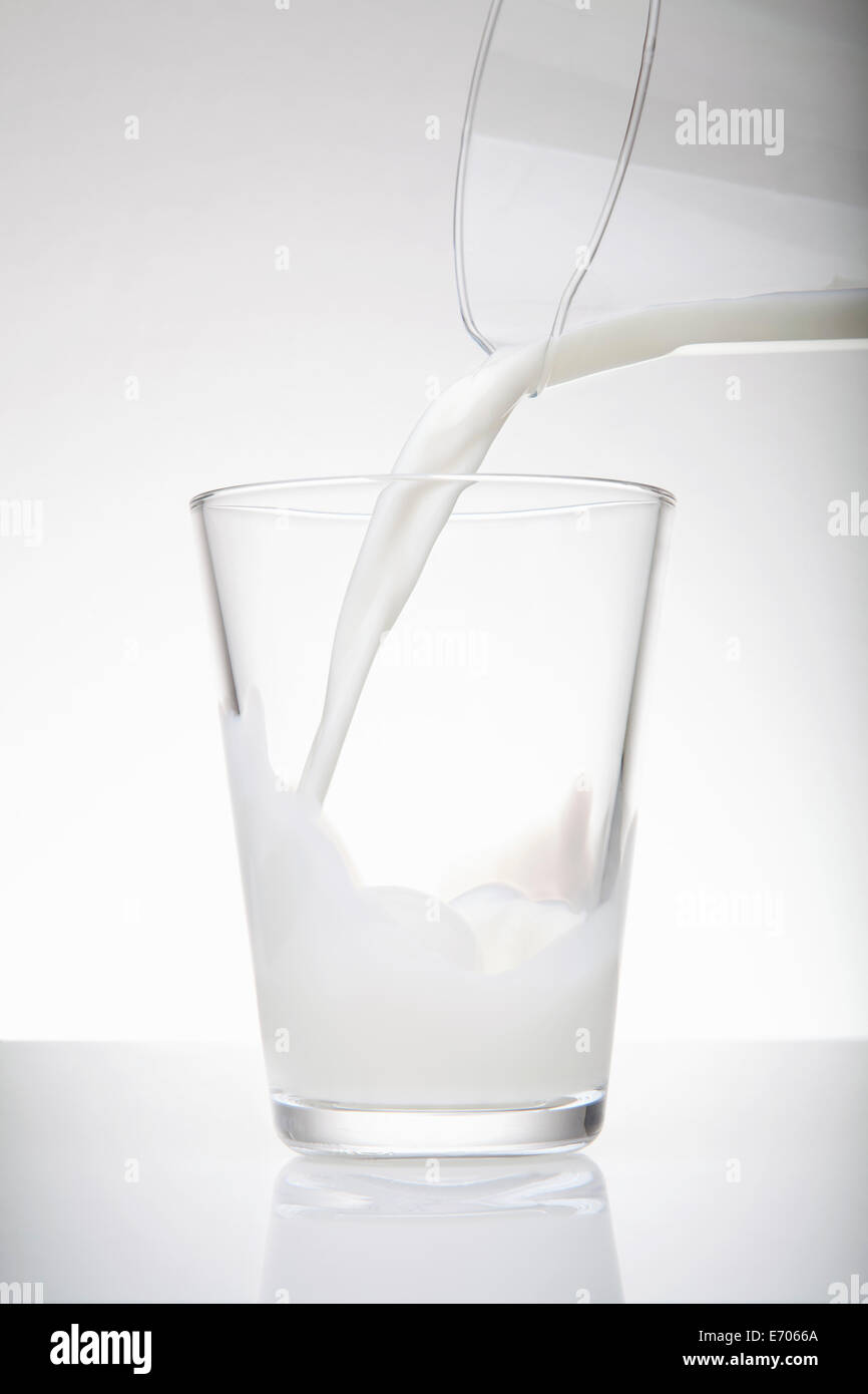 Verter la leche fresca de jarra en vaso Foto de stock