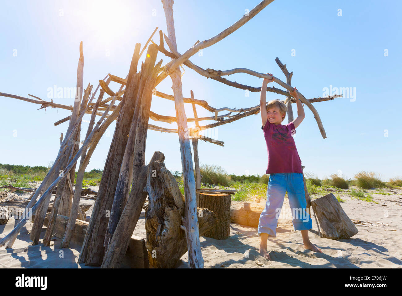 Boy levantamiento driftwood a construir viviendas, Playa Caleri, Veneto, Italia Foto de stock