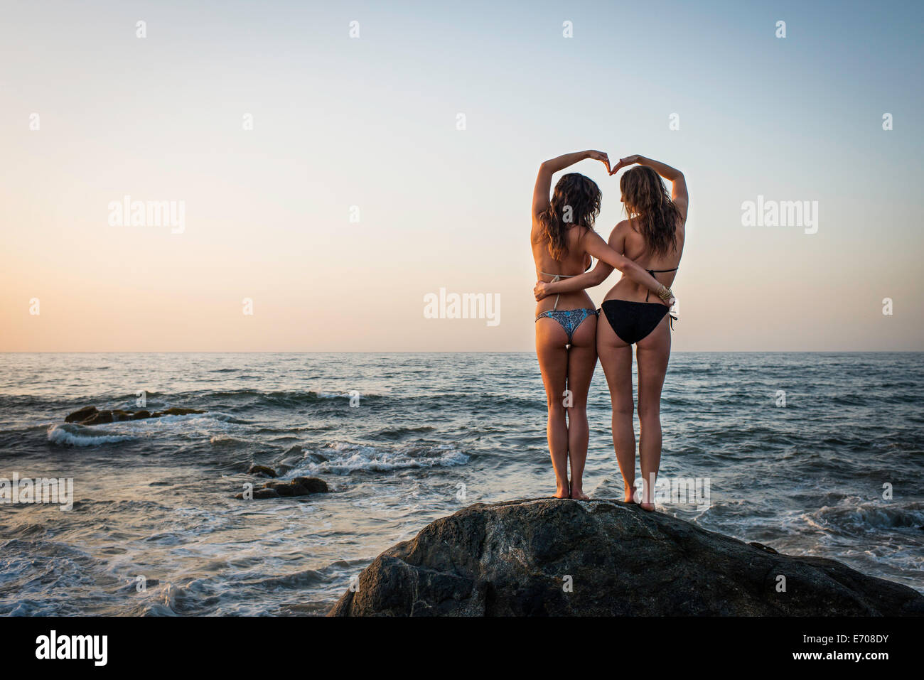 Dos jóvenes mujeres de pie sobre una roca en el océano, vista trasera Foto de stock