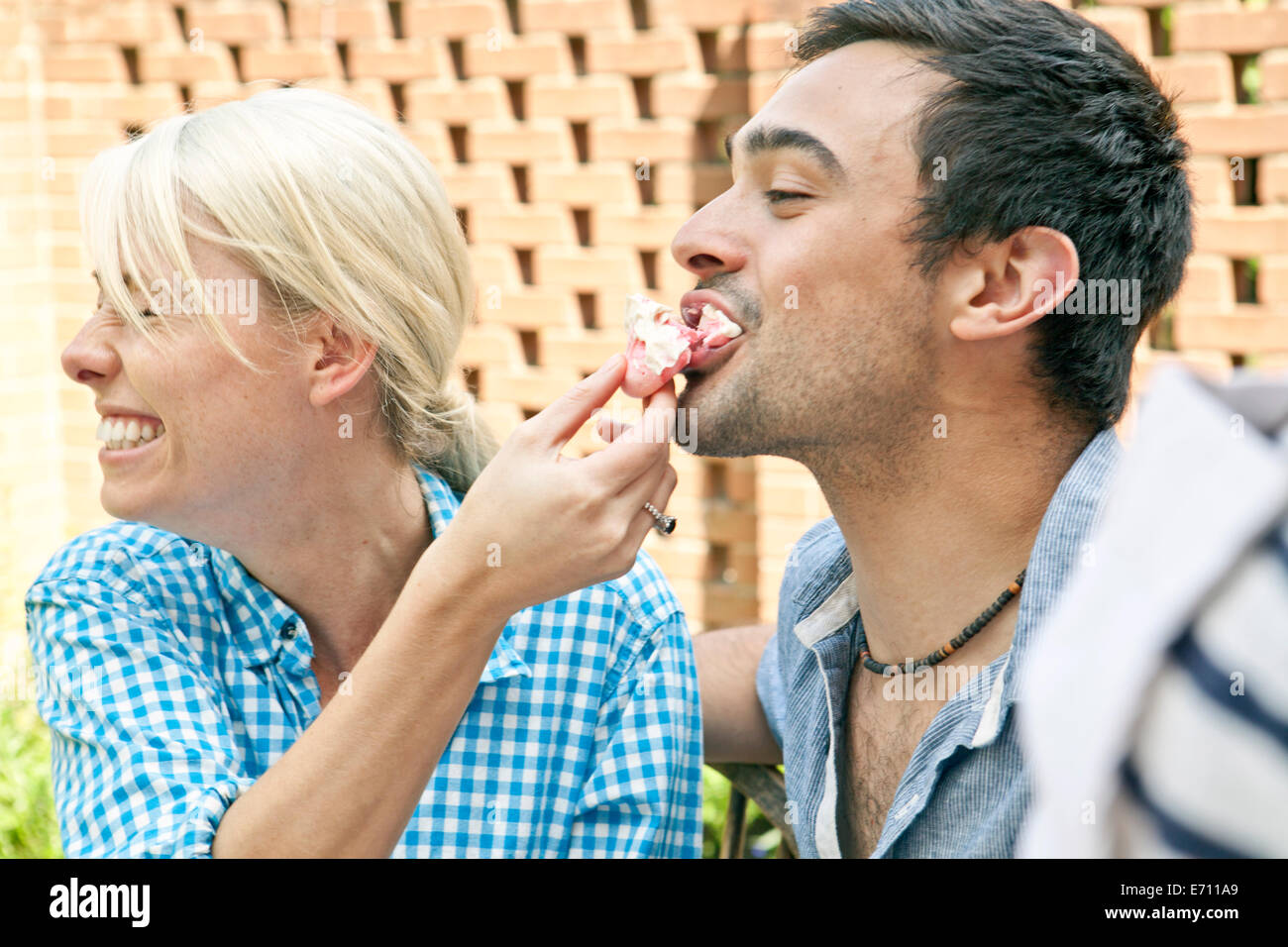 Pareja joven alimentándose de merengues en garden party Foto de stock