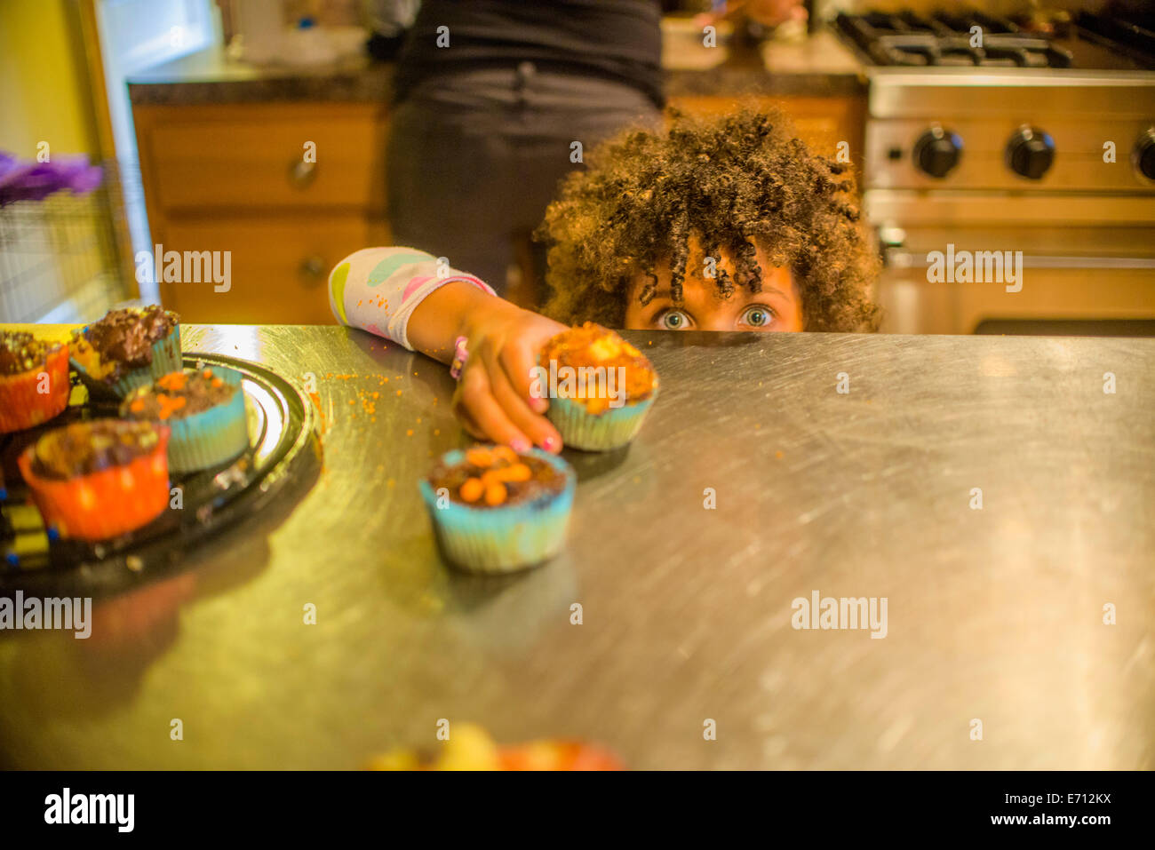 Retrato de niña alcanzando pastelitos en la cocina Foto de stock