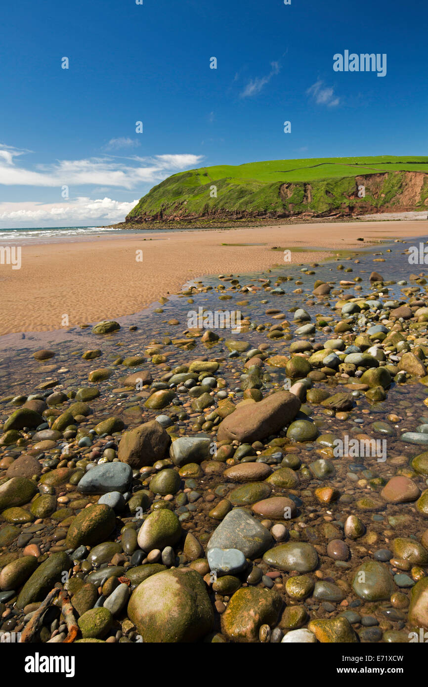 Desierta playa de guijarros y arena a los pies de los acantilados cubiertos de hierba verde y azul cielo en la localidad de St Bees Cumbria Inglaterra Foto de stock