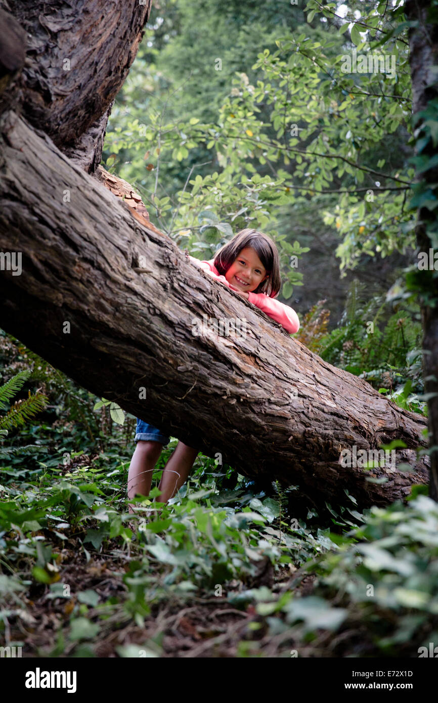 Retrato de niña sonriente (6-7) apoyándose contra el tronco del árbol en el bosque Foto de stock