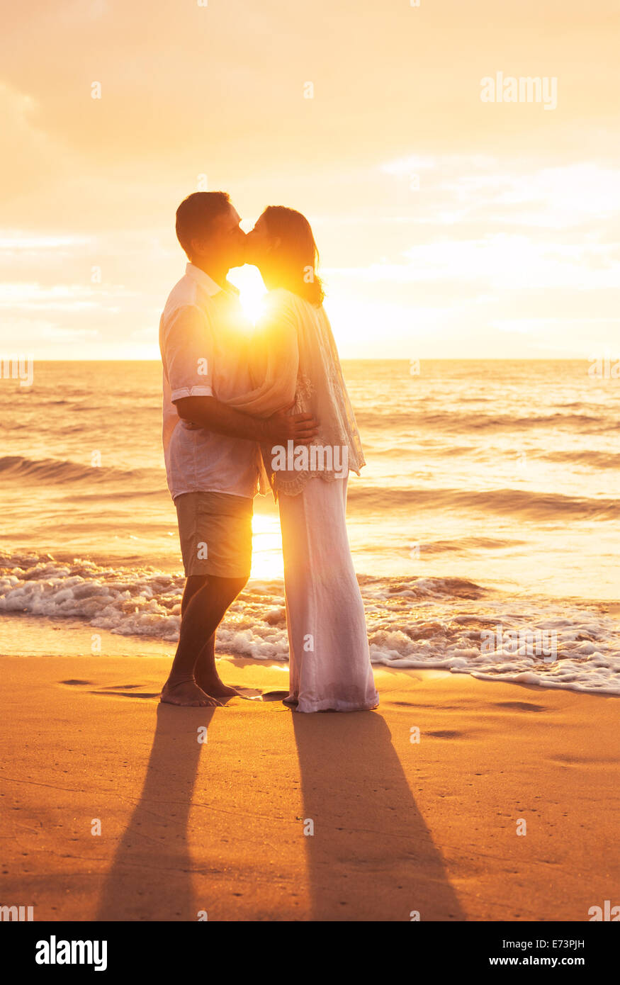 Romántica pareja besándose al atardecer en la playa Foto de stock