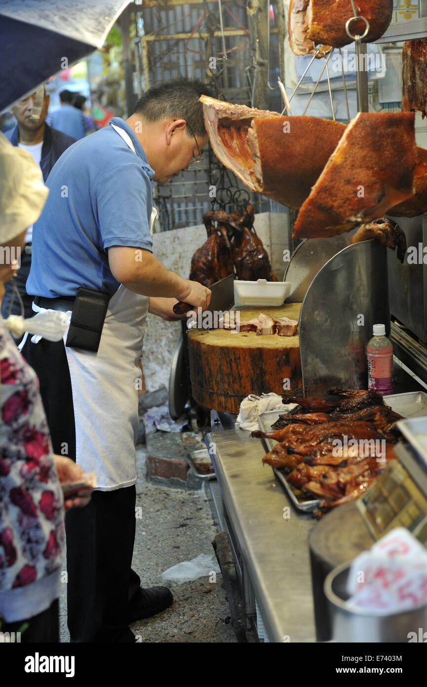 El hombre cortando chuletas de cerdo en acera carnicería, Kowloon, Hong Kong, China Foto de stock