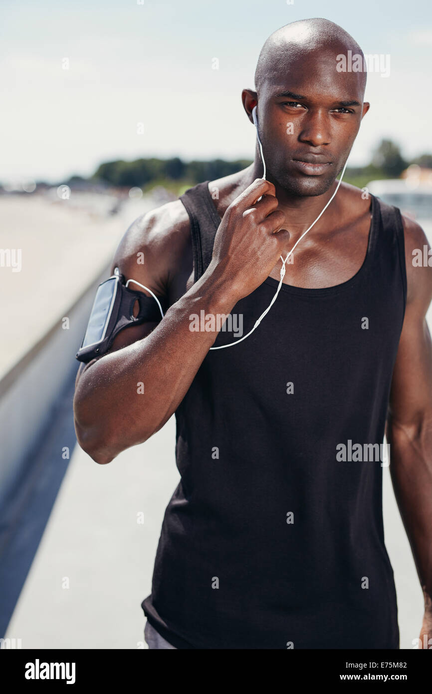 Retrato de colocar joven afuera escuchando música en auriculares. El hombre muscular sano con banda de brazo. Foto de stock