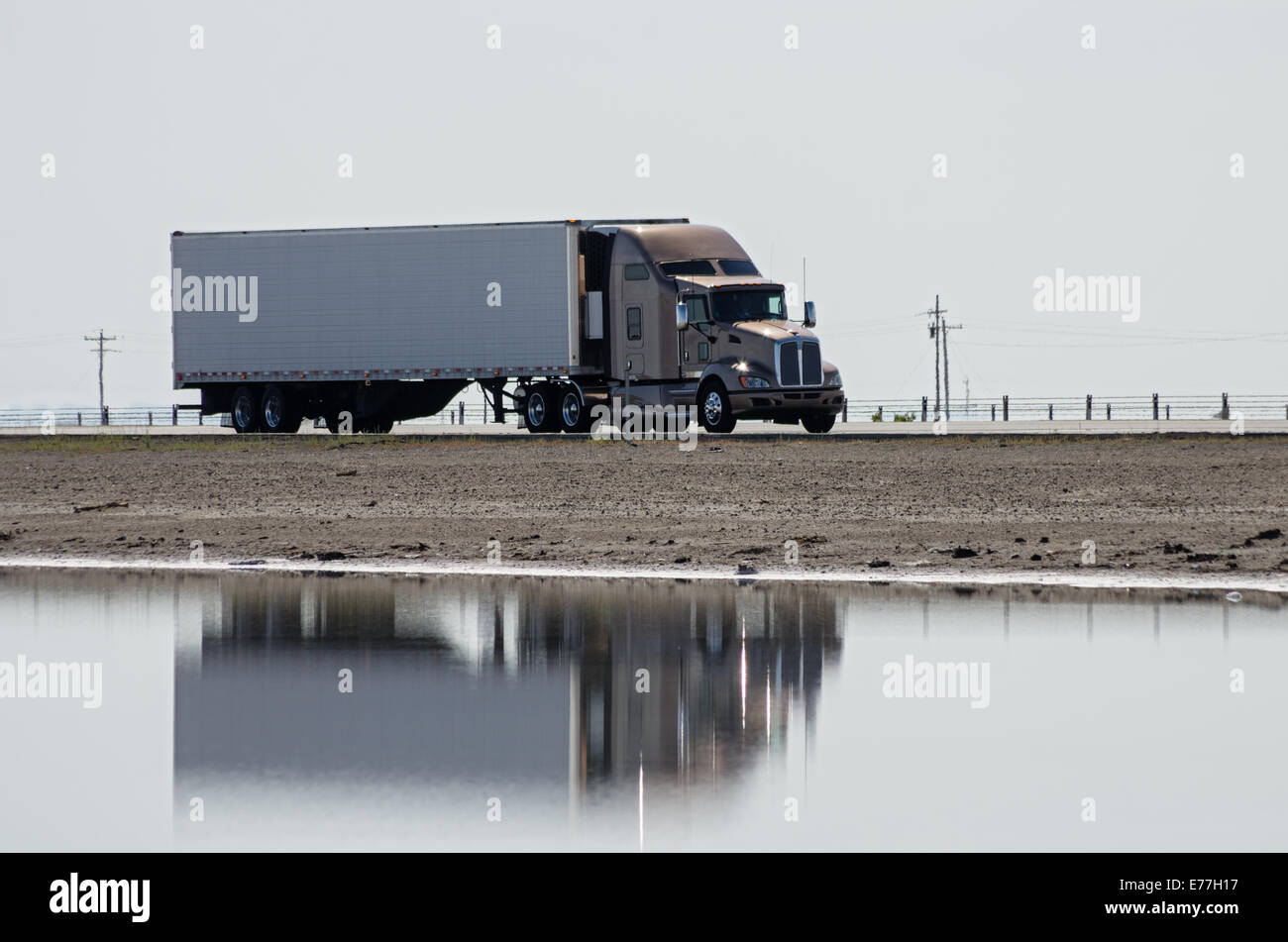 Tractor semi remolque camión conducir por una autopista Causeway con reflejo en el agua Foto de stock