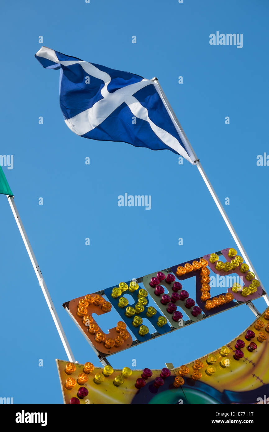 La Saltire, la bandera nacional escocesa en la cima de un mástil colocado por encima de la palabra loco escrito en multicolores luces de feria Foto de stock