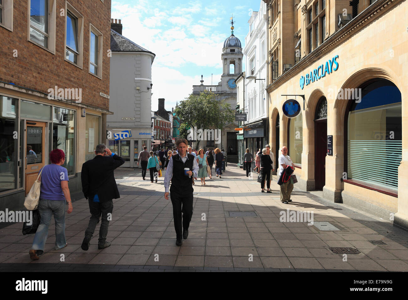 El hombre lleva un café para llevar y otros peatones en una calle del centro de la ciudad de Norwich a la hora del almuerzo. Foto de stock