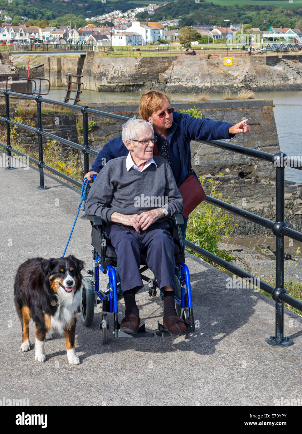 Una hija señalando los lugares de interés turístico del puerto de Burry Port, Gales, a su anciano padre discapacitados en silla de ruedas Foto de stock