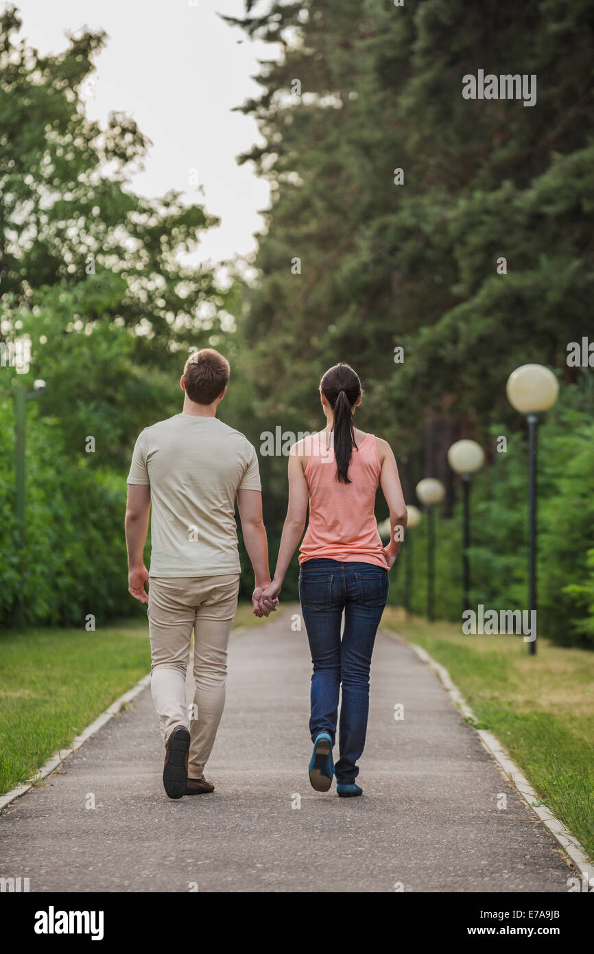 Vista trasera de la joven pareja caminando mientras mantiene las manos en el parque Foto de stock