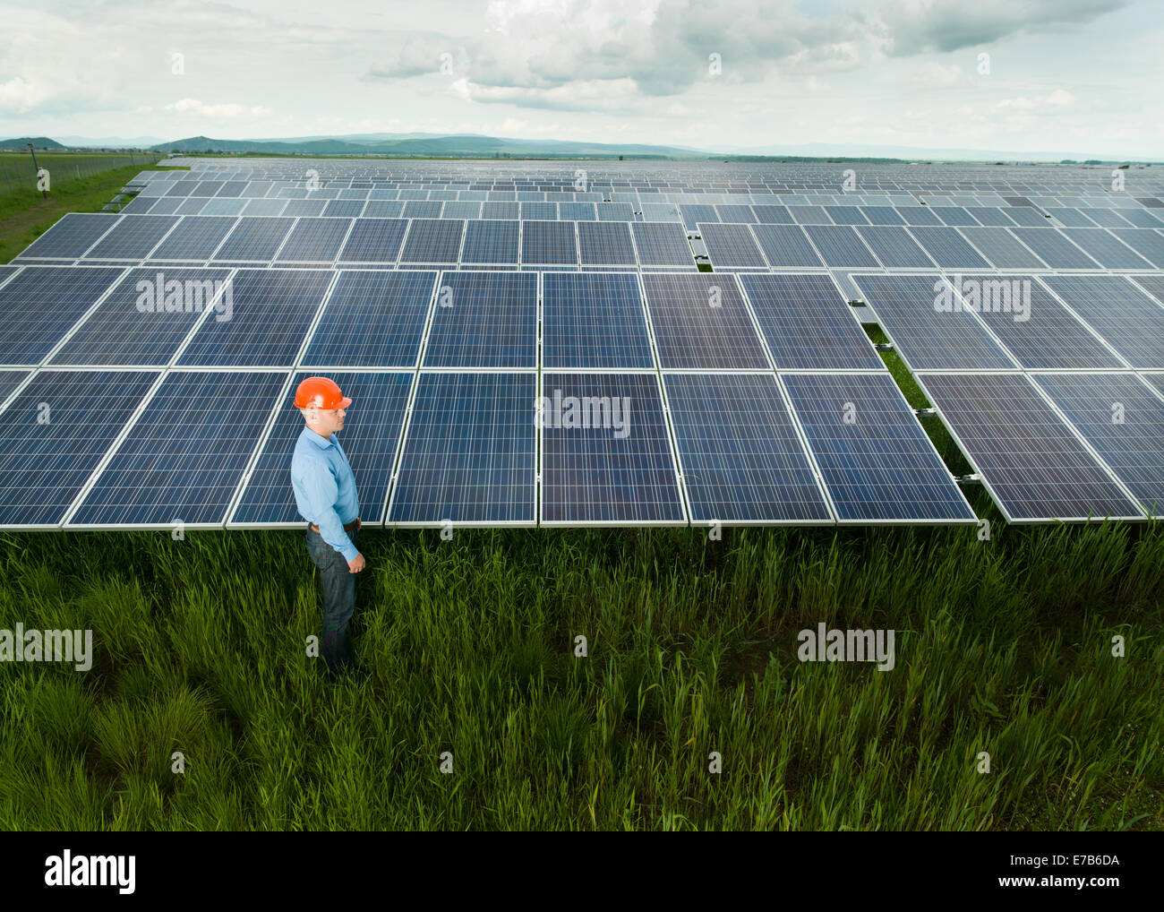 El hombre vestido con ropa y equipamiento técnico de pie cerca de los paneles solares, al aire libre, con el cielo nublado Foto de stock